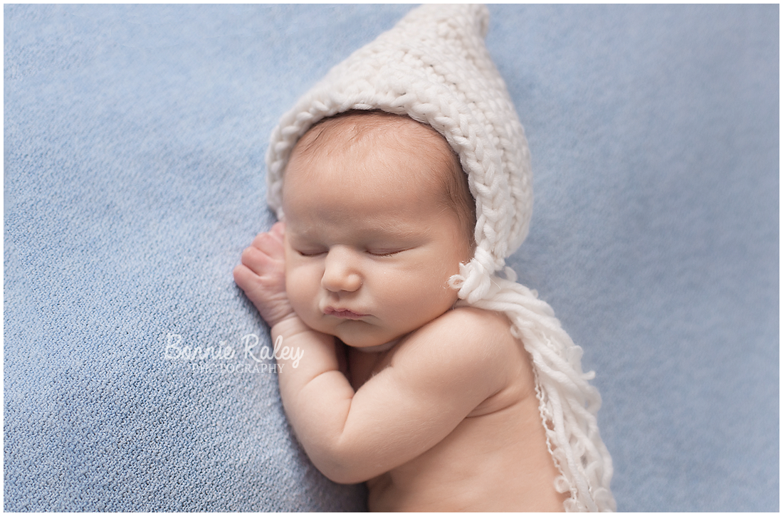 newborn baby boy on blue blanket with cream bonnet {main line newborn photographer}