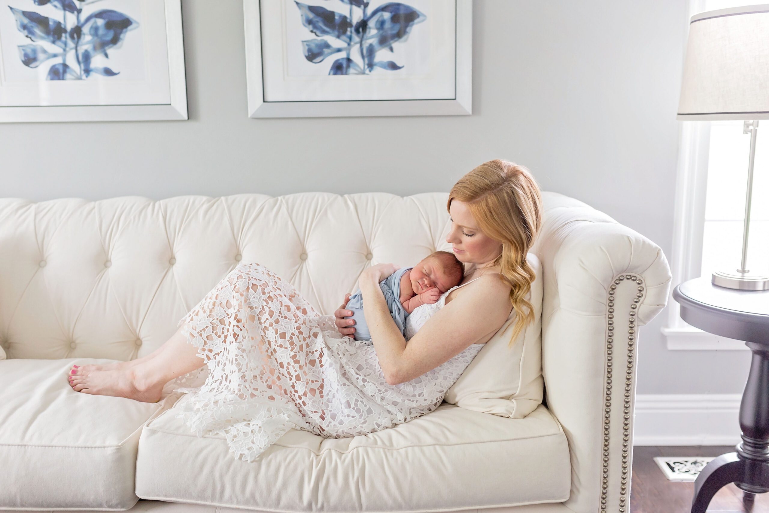 Mother holding newborn baby on white couch during in-home lifestyle newborn photography session in West Chester, PA