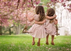 Spring family photo session in the Main Line PA with two young sisters sitting on a swing under pink cherry blossoms.