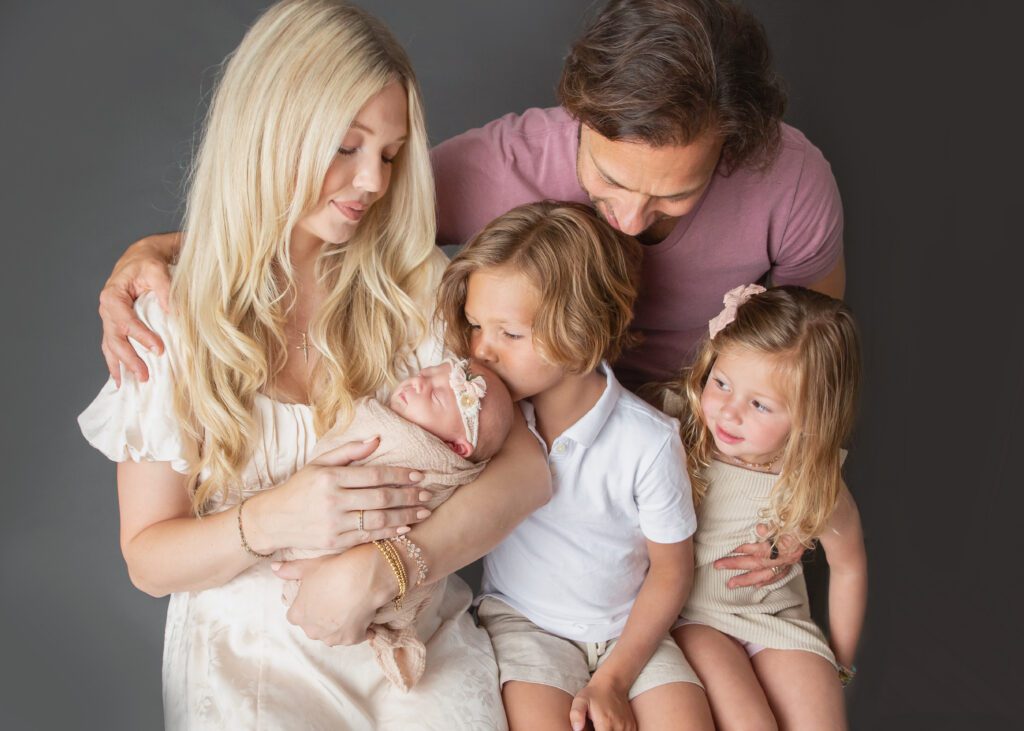 Family of five in coordinated neutral and blush outfits during posed newborn photography session in Philadelphia